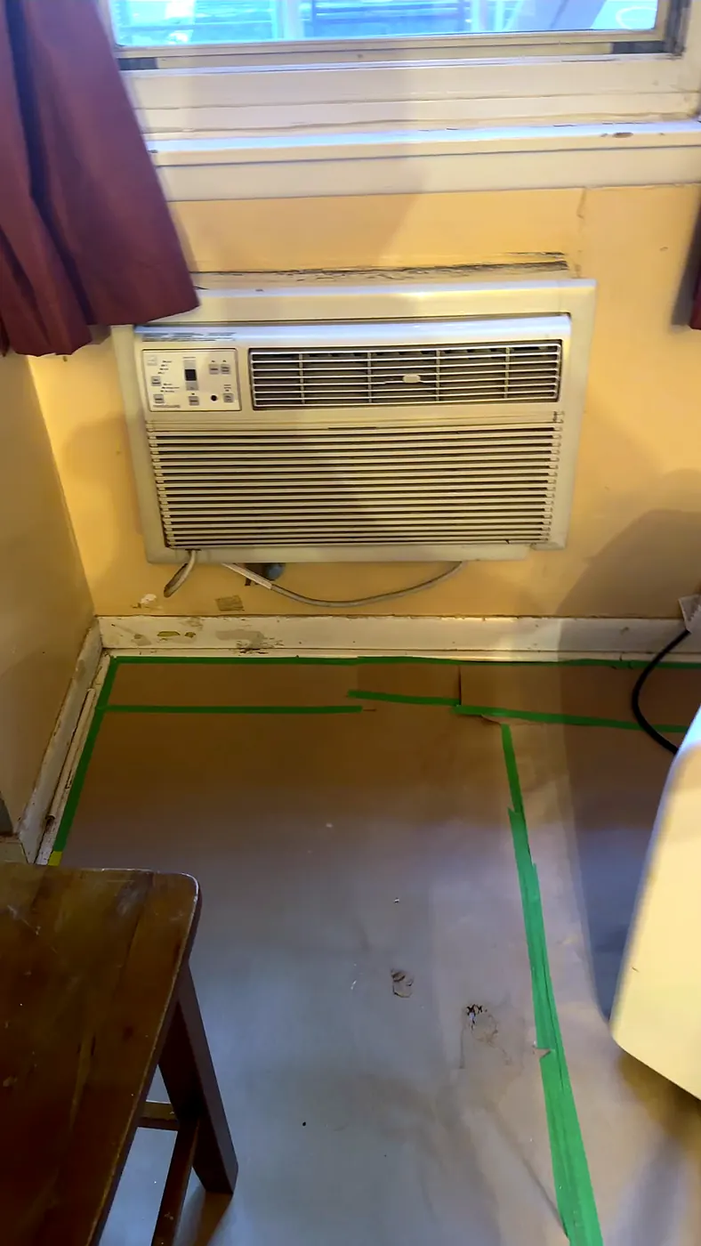 Old through-wall air conditioner under the living room window, floor papered for demolition