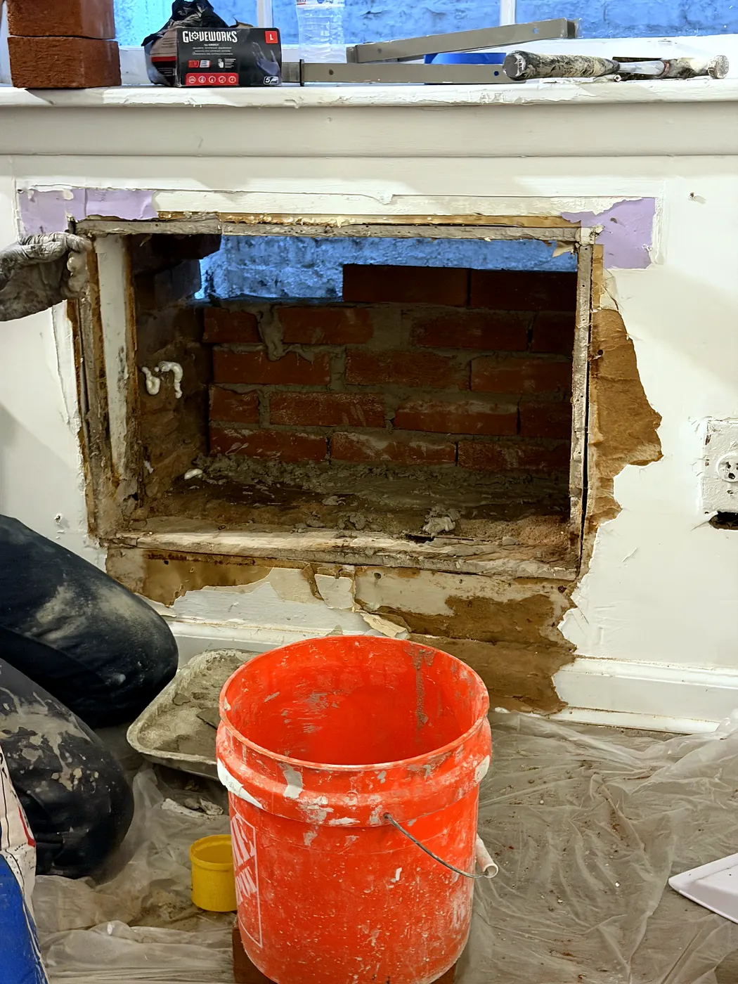 The AC opening being bricked up with new brick and mortar, bucket and trowel in front