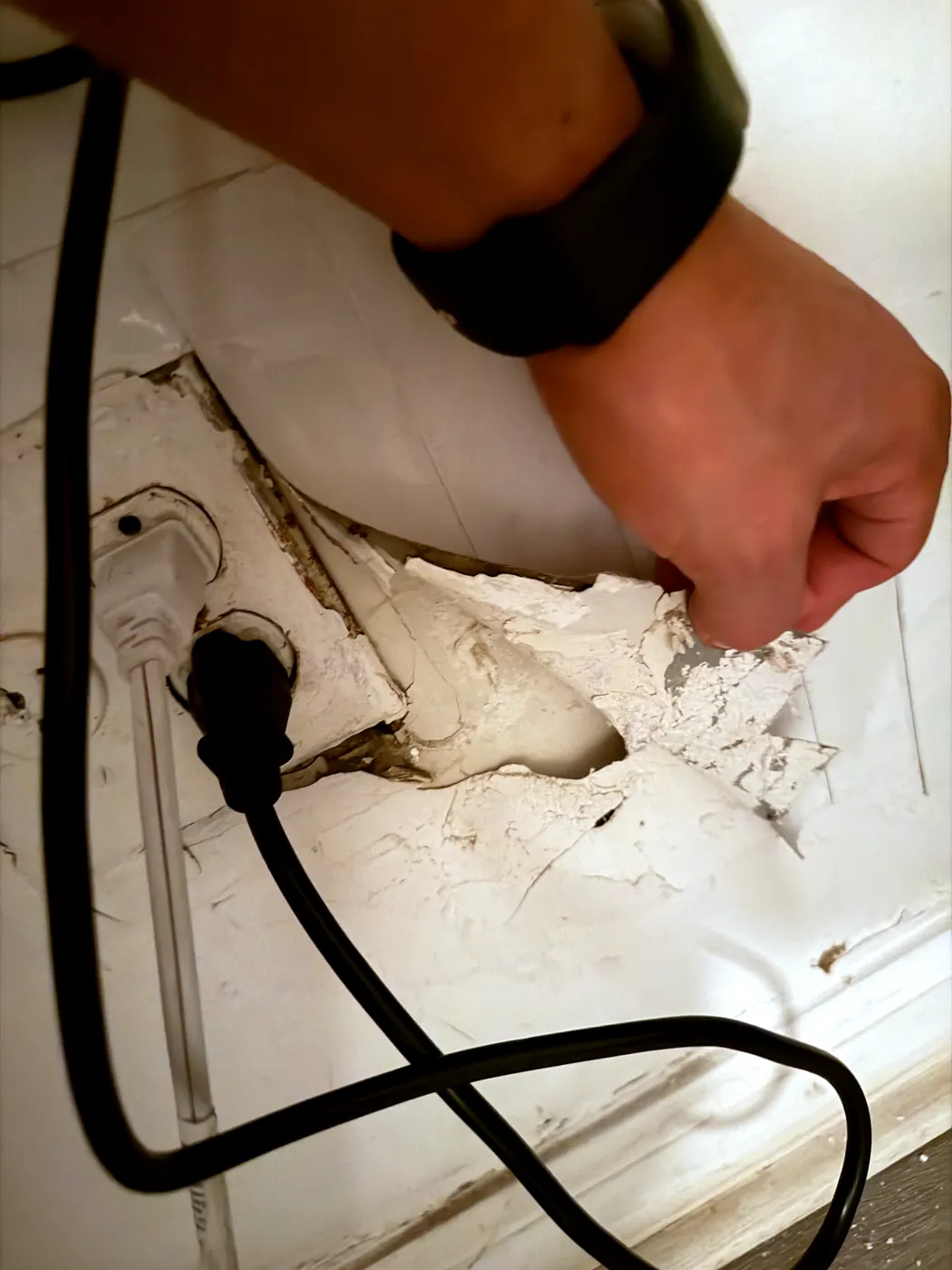 Hand pulling loose plaster away from the wall beside the old AC outlet