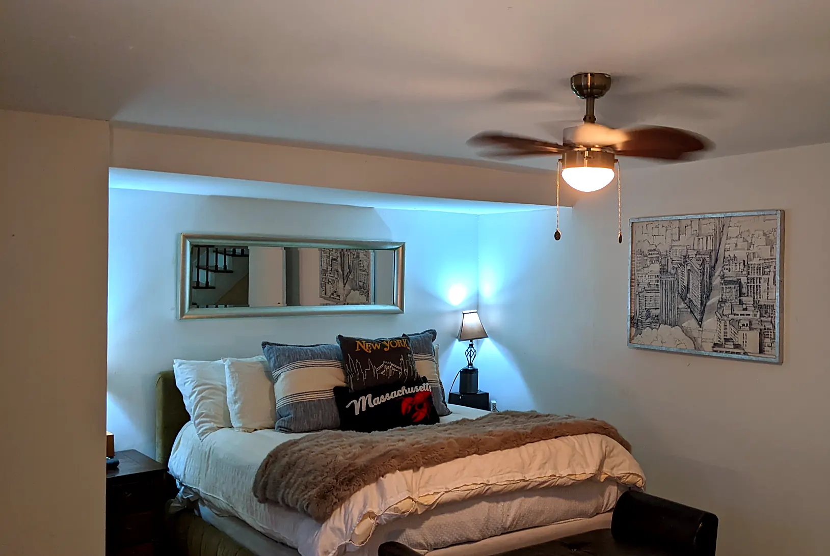 Main bedroom in 2022: green upholstered bed, city pillows, blue light
