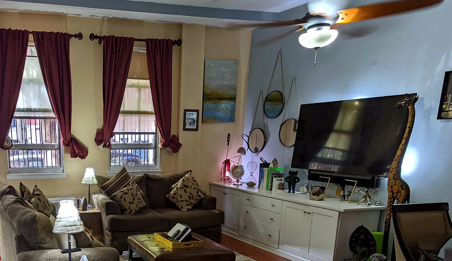 TV wall in 2022: blue wall, brown sofas, leather ottoman, crowded shelf
