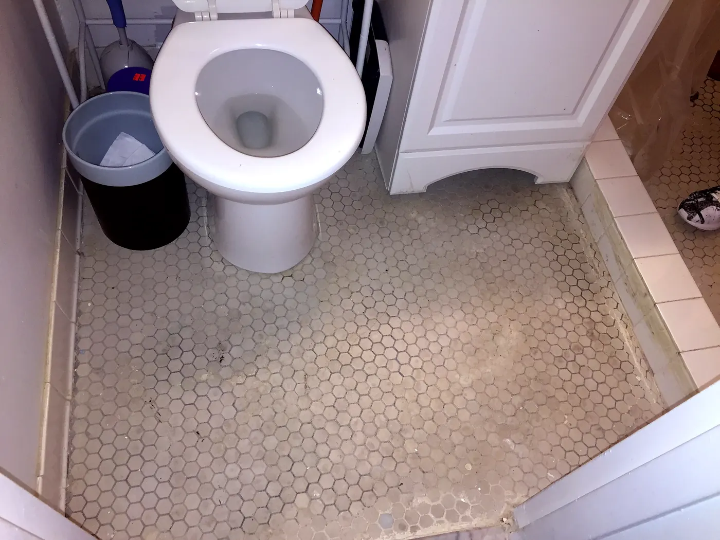 The bathroom in September 2015: hex floor, toilet, and a vanity cabinet with no countertop